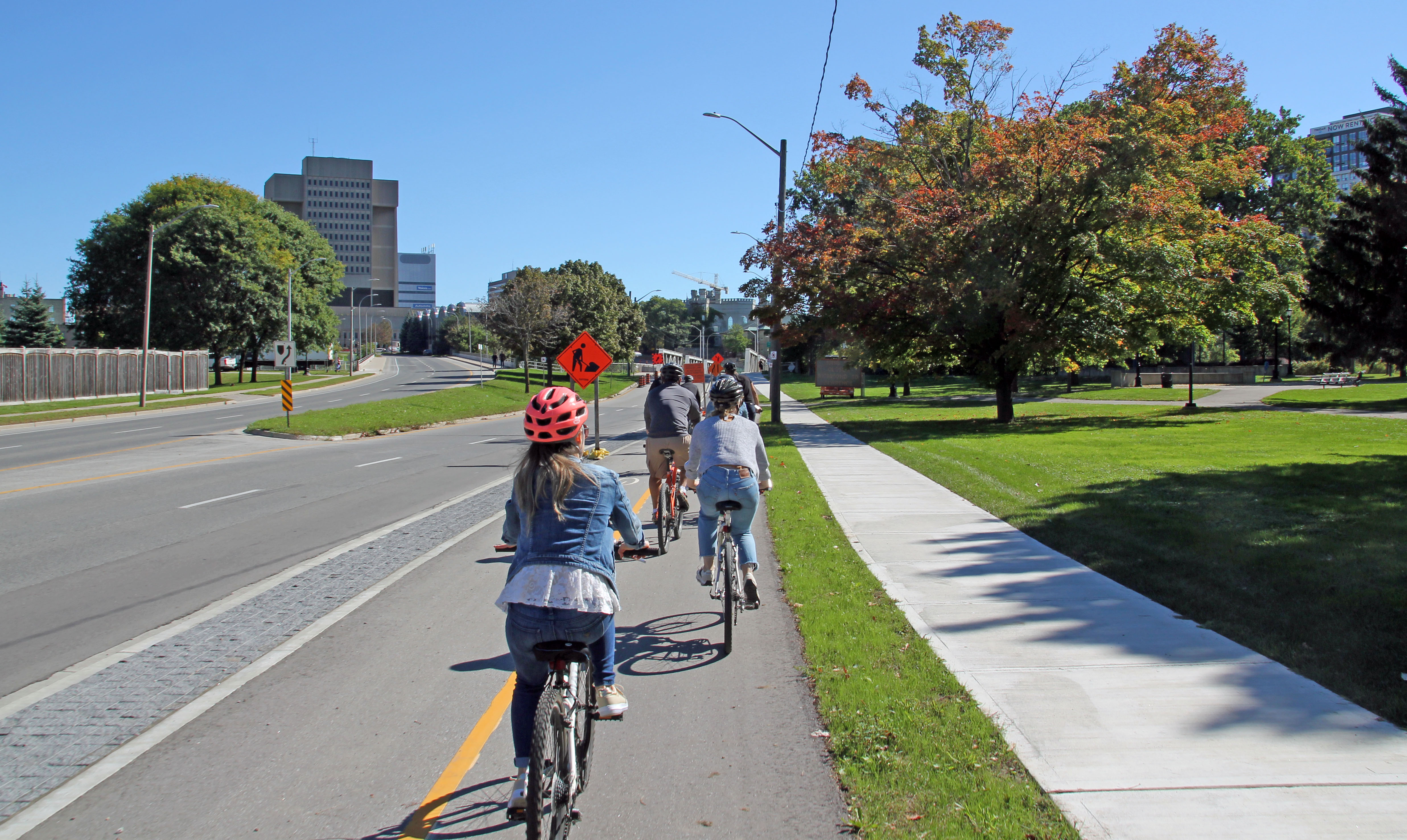 A group of people ride their bikes in a separated bike lane along Riverside Drive towards downtown. 