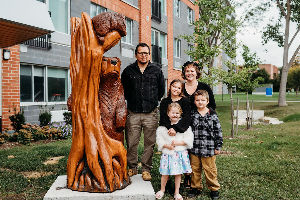 Garrett Nahdee and his family of five pose beside the Owl Family artwork. 