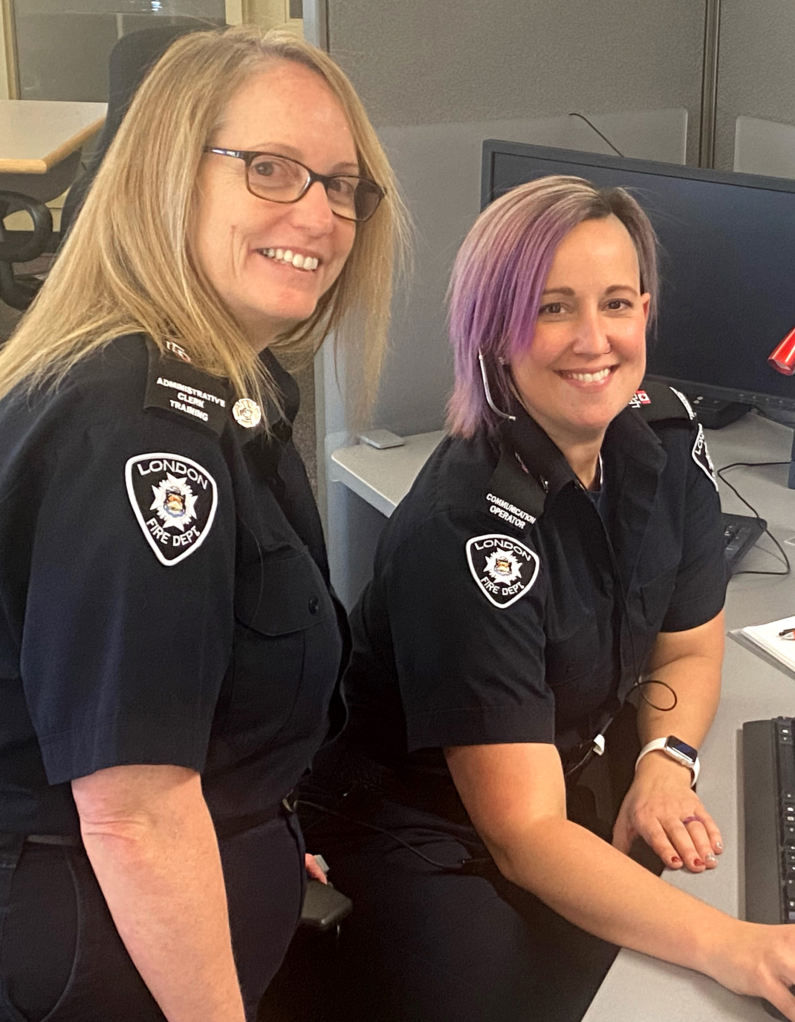 Two female firefighters at a desk smiling for the camera