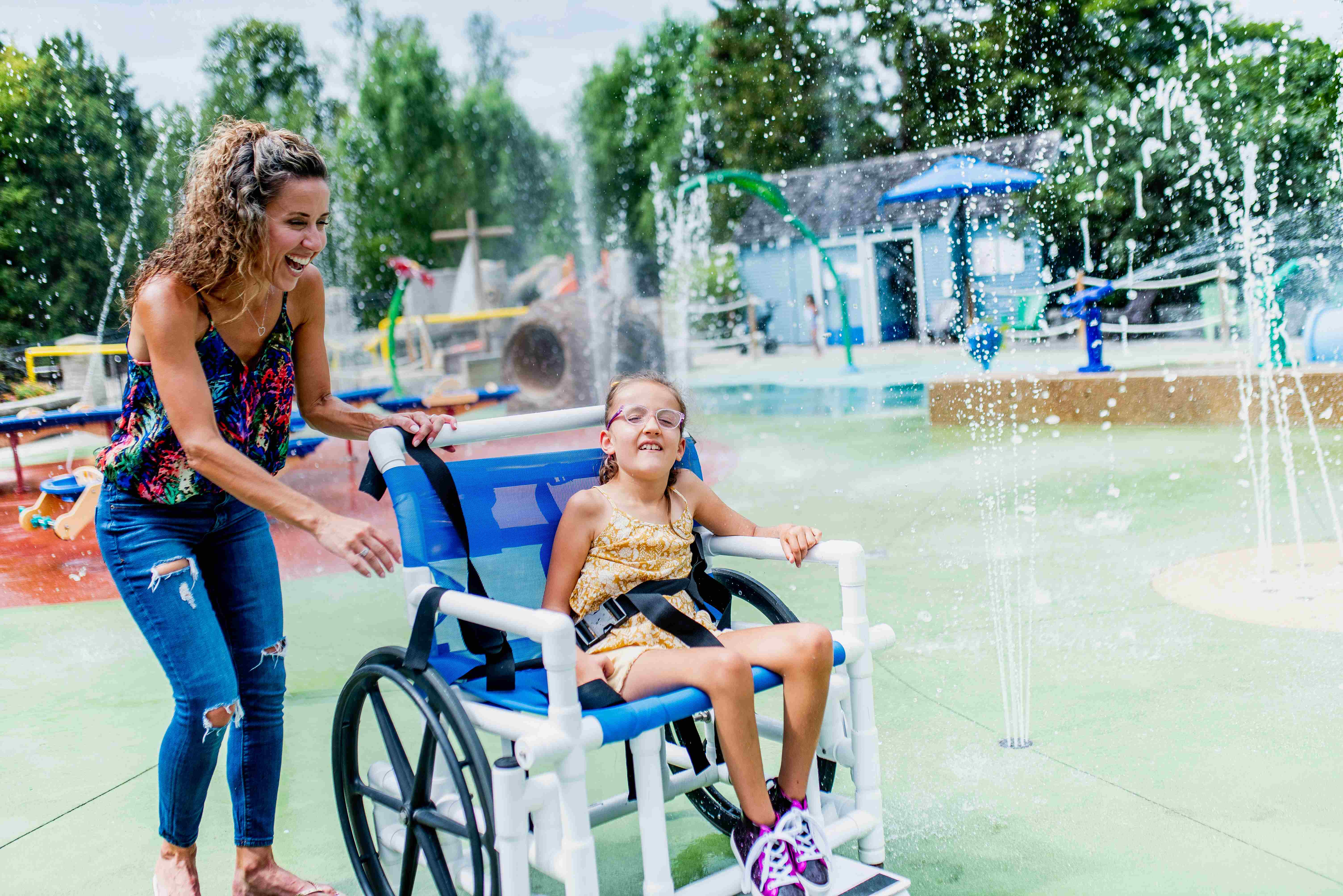 Young girl in wheelchair with mother pushing her at the Storybook Gardens' splash pad