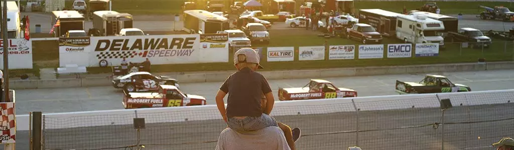 Child on their parent's shoulders watching a race car