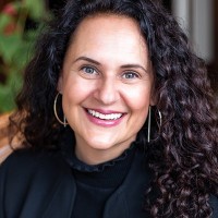 Woman with curly hair and earrings smiling at camera