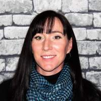 Woman in scarf smiling at camera in front of brick wall