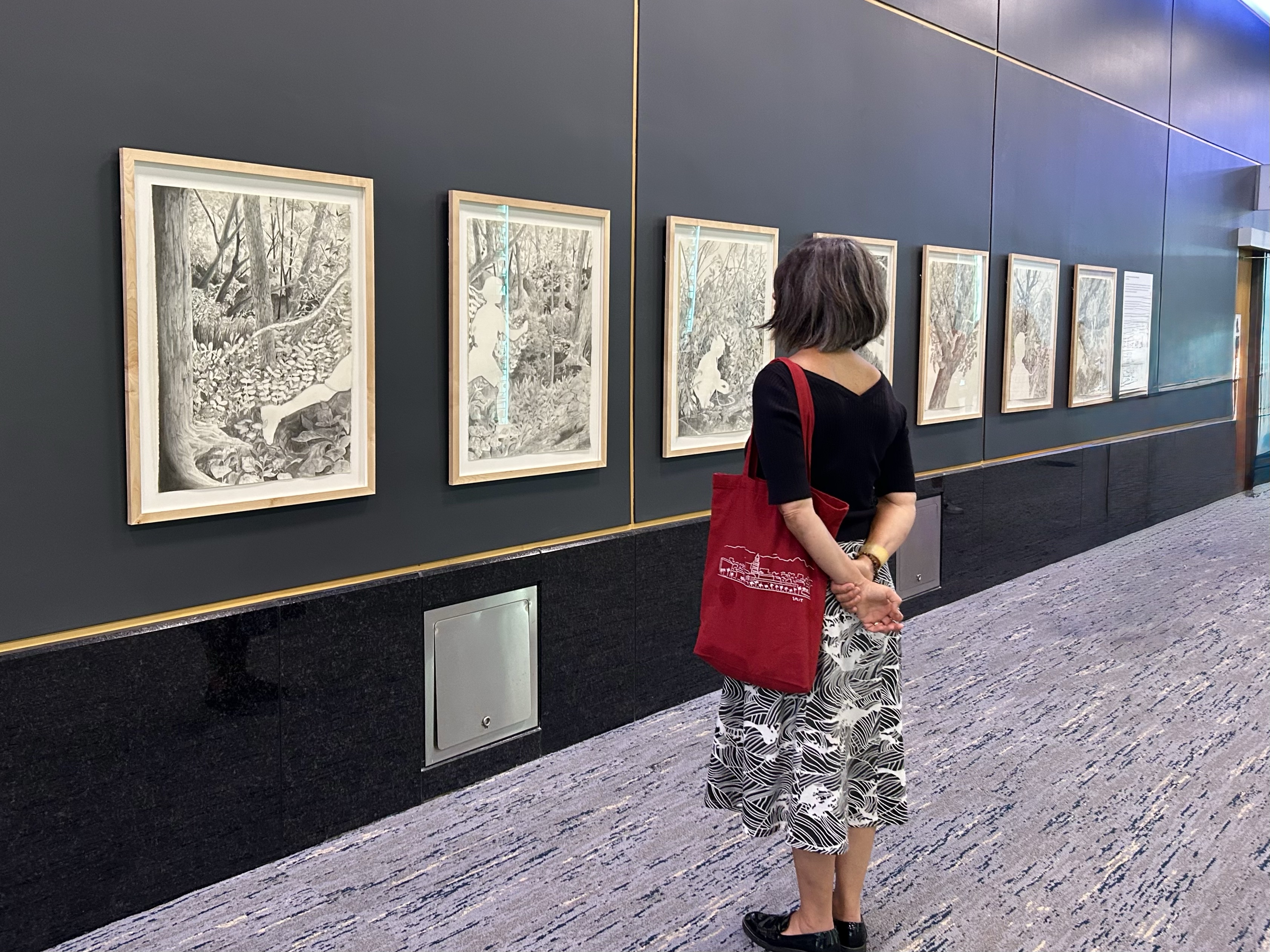 A woman views a series of drawings on a wall