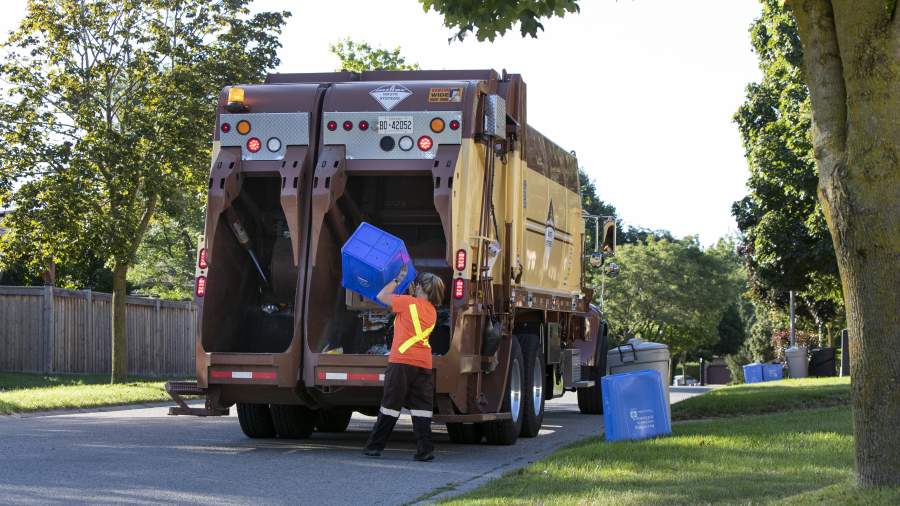 A recycling operator unloads a full blue bin into a recycling truck. 