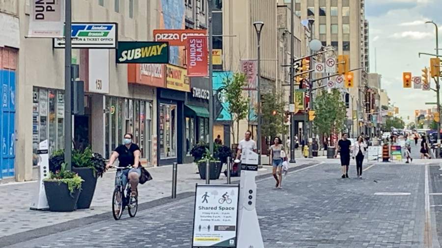 Dundas place road closure in effect. Signage in place on the street reminding Londoners that this is a shared space. Cyclist biking down the street with a face mask on. 