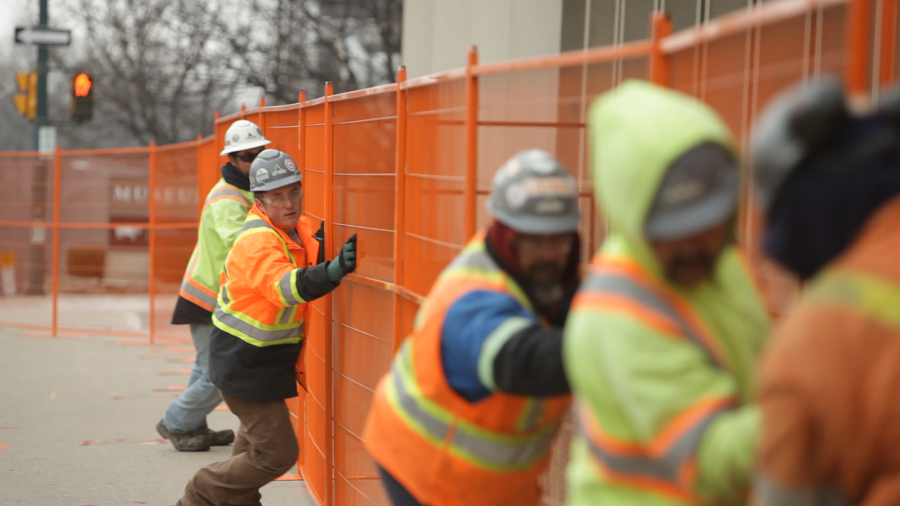 A group of construction workers move an orange construction fence together outdoors. 