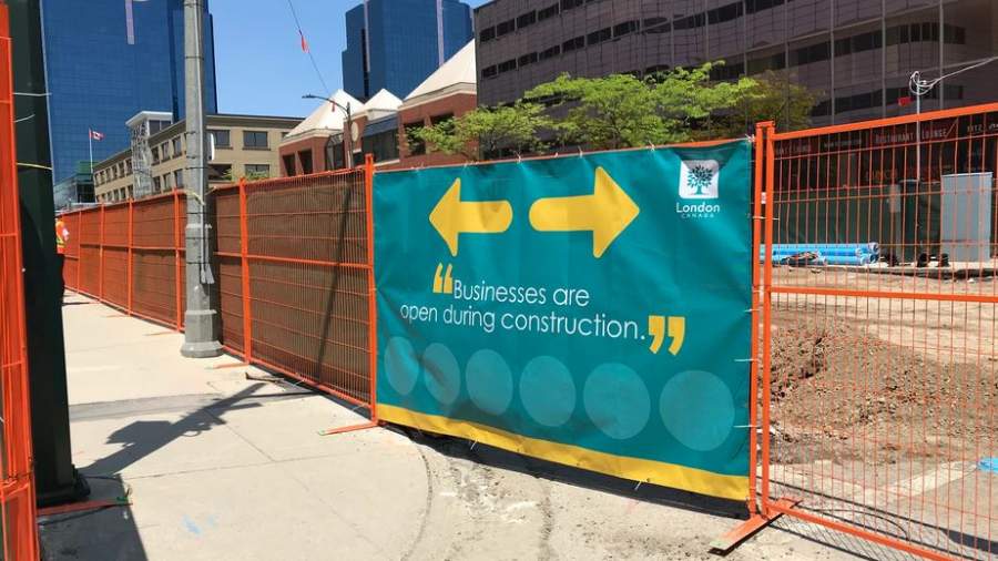 A sign on the construction fencing showing businesses are open on Dundas Place. 
