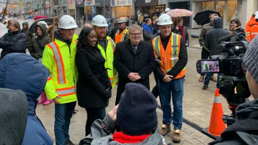 A crowd of construction workers pose for a photo with Mayor Holder and Councillor Kayabaga on Dundas Place