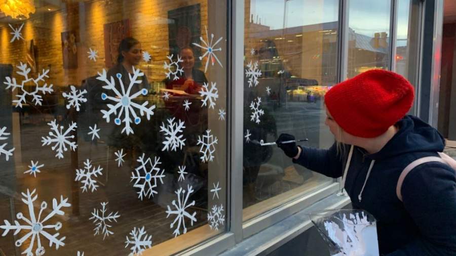 An artist paints snowflakes on windows on Dundas Place