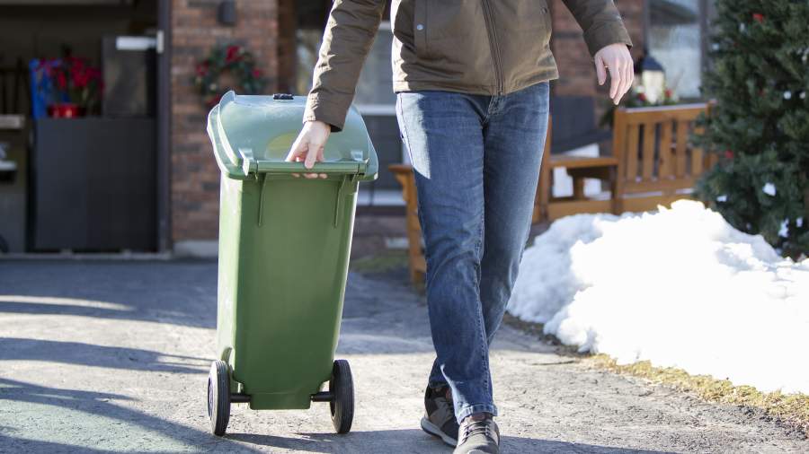 A medium sized Green Bin is rolled to the curb my a resident on a sunny day. 