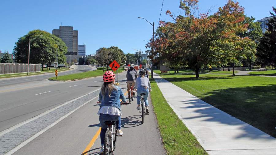 Several people ride bikes on a separated bike lane on Riverside Drive in London, Ontario. 