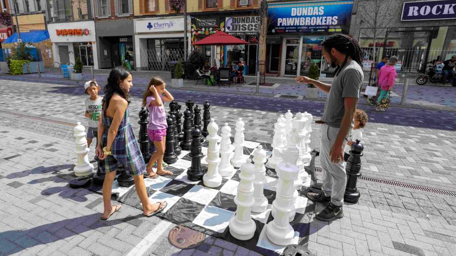 A family playing chess on Dundas Place using a giant chess board. One player is pondering his next move. 